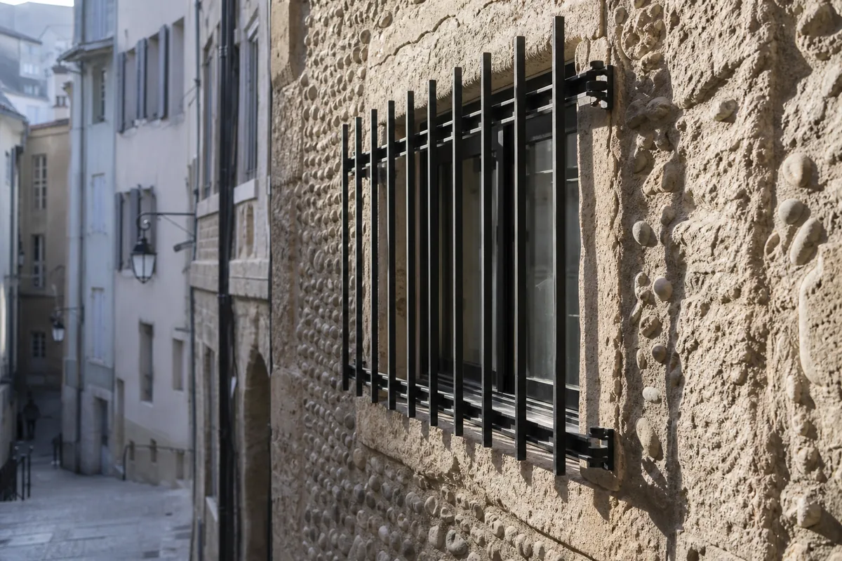 Grille en acier noir mat sur mesure devant une fenêtre basse d&rsquo;un mur de molasse claire