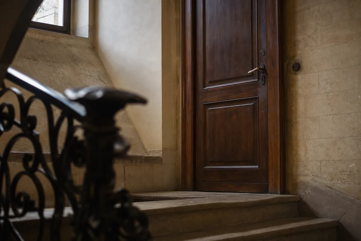 Ancienne porte palière en bois massif dans une cage d&rsquo;escalier de pierre claire
