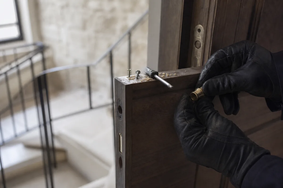 Mains gantées ajustant un cylindre européen sur une porte palière en bois plein d&rsquo;un immeuble ancien